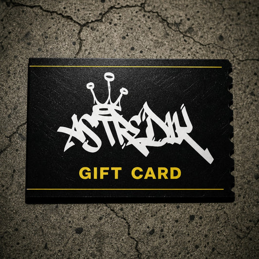 Cartão presente digital astredik preto com logótipo em graffiti branco e detalhes em amarelo sobre fundo de cimento.