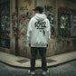 Homem de costas usa hoodie branco astredik com estampa 1312 em beco urbano com grafites