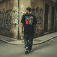 Homem de costas a usar t-shirt preta astredik com estampa gráfica estilo banda desenhada numa rua com graffiti